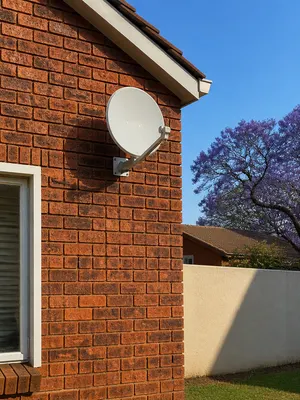 Satellite dish wall-mounted on a face-brick suburban home